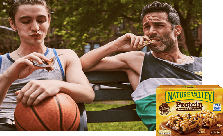 woman and man sitting on a bench outdoors and snacking on Nature Valley granola bars